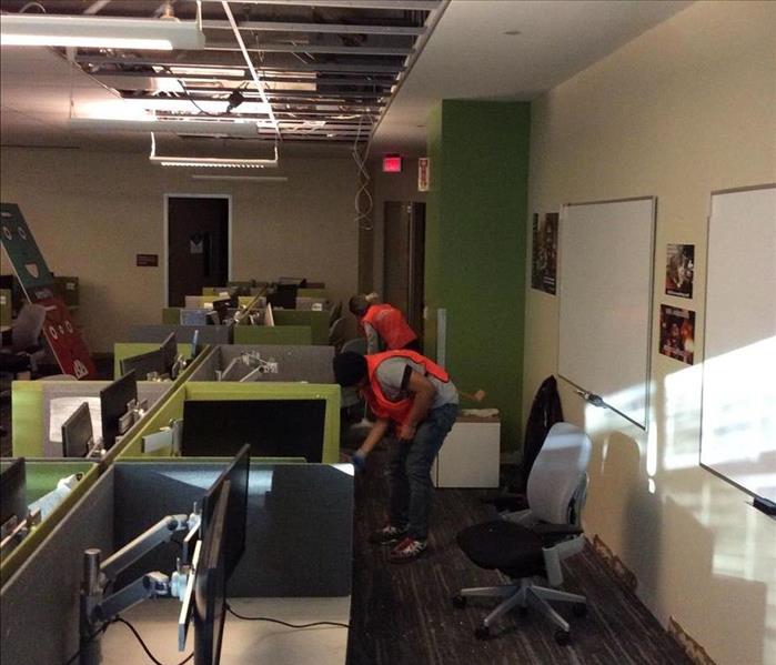 Same office area, debris cleaned up off the floor and desks, ceiling tiles removed, 2 employees cleaning