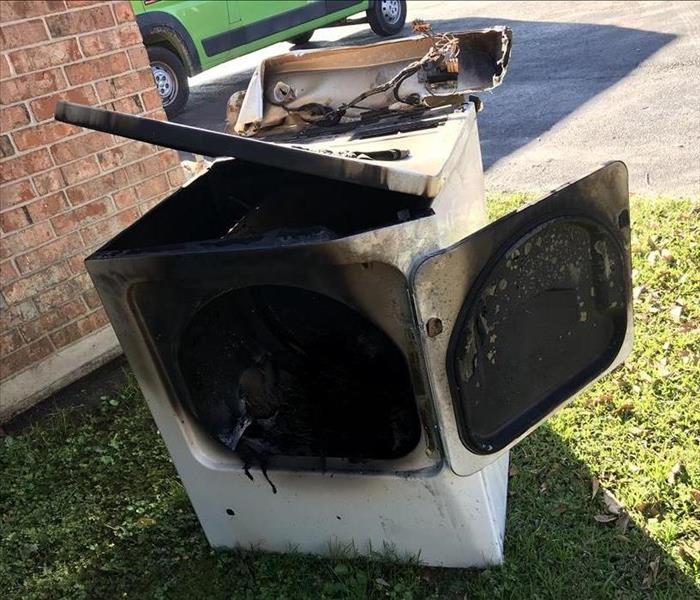 dryer outside of house in the grass with fire damage. 