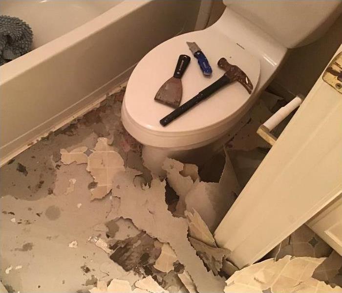 bathroom floor with laminate flooring pulled up and pieces scattered everywhere, toilet to the right, bathtub in top corner
