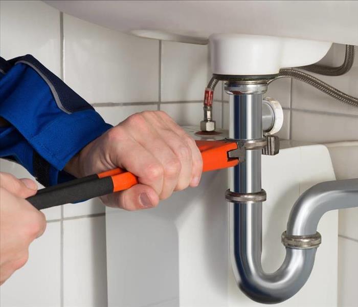 picture of sink pipe, man using a tool on the pipe to adjust a fitting. 