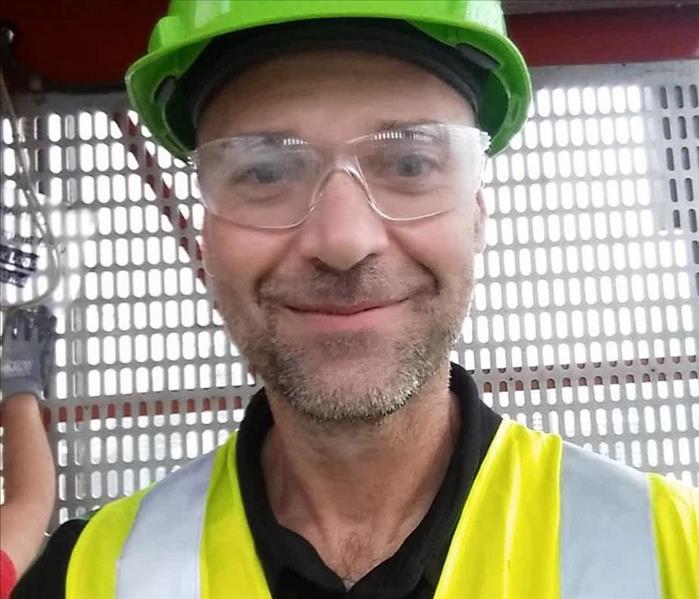 selfie of man wearing yellow safety vest, green safety helmet, and safety goggles. 
