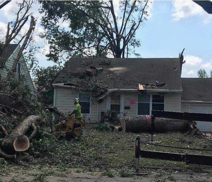 House with trees fallen down in yard, roof damaged with tree debris on top